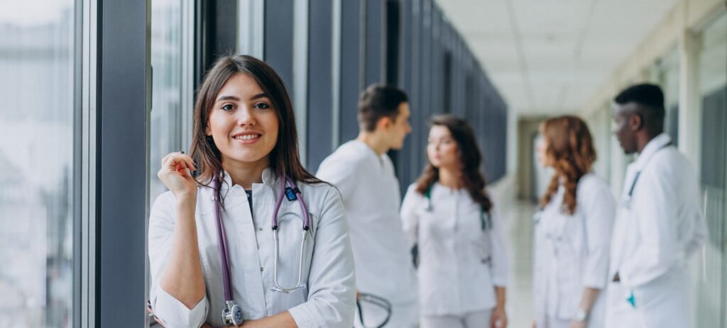 alt="MBBS student in vietnam medical college standing in a corridor of the hospital, wearing a white coat and stethoscope
