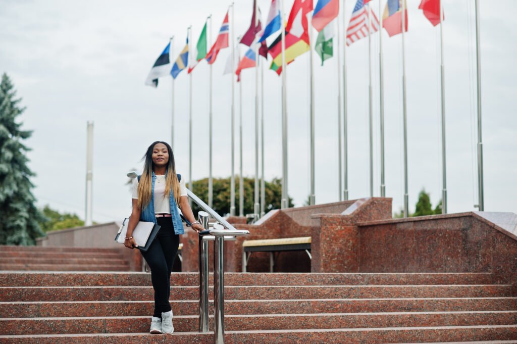 alt=*Study in Tajikistan African student female posed with backpack and school items on yard of university,