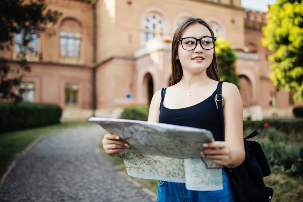 alt=*Study in Philippines portrait of happy young girl bring backpack looking for something and hold map travel in unknown city